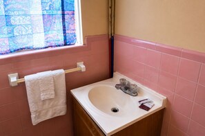 A bathroom with a white sink, a towel rack with a white towel, and a window with patterned curtains.
