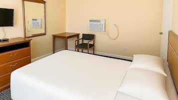 A hotel room with a bed, a desk, a chair, a dresser, a mirror, and a wall-mounted air conditioning unit.
