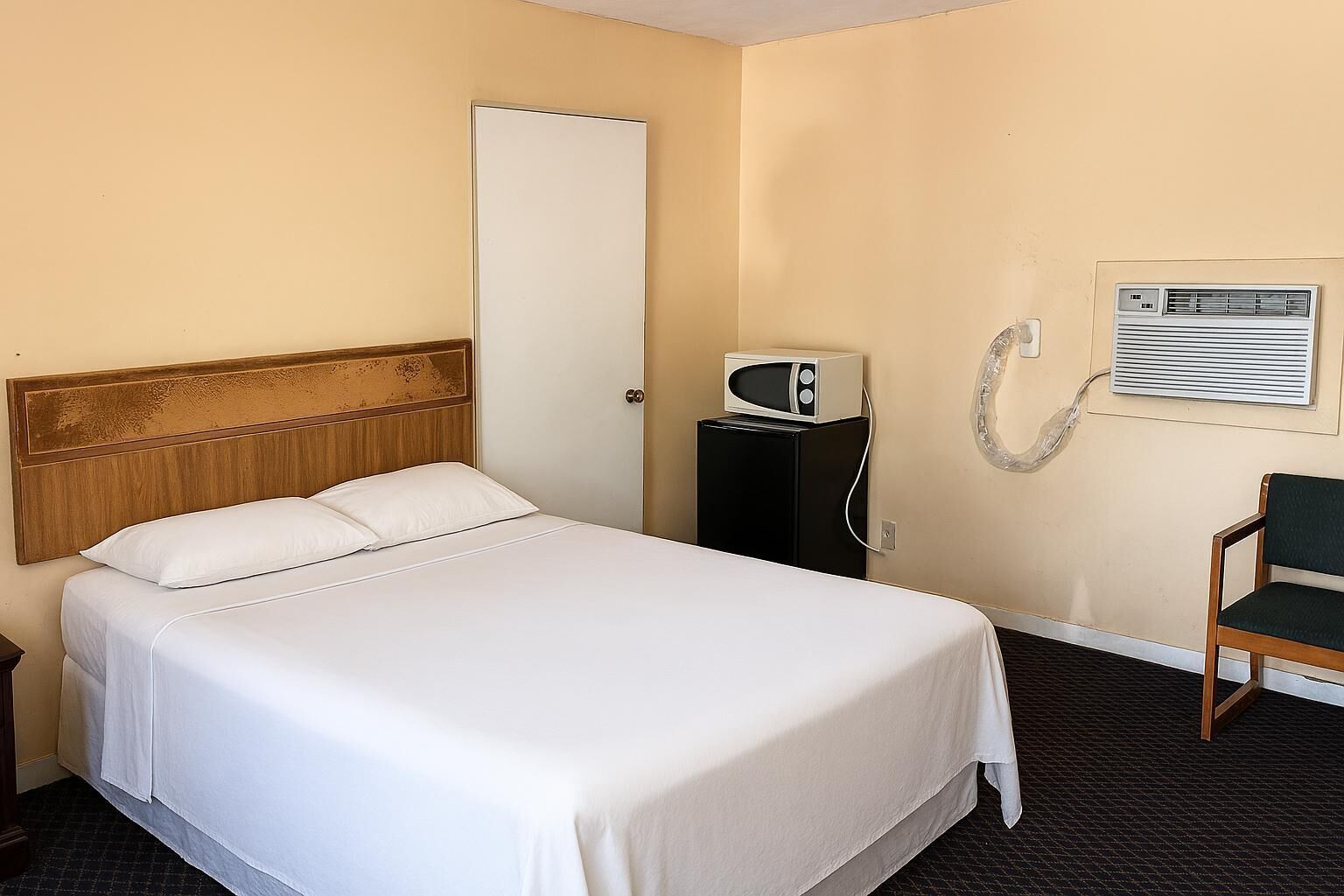 A hotel room with a bed, a microwave, a chair, and an air conditioning unit.