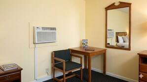 Ett hotellrum med en trästol, ett litet bord, en spegel och en väggmonterad luftkonditioneringsanläggning.