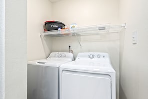 A laundry area with two white washing machines, a shelf with detergent, and a power outlet. - First Floor 3 BR Condo ~ Newly Renovated, Sleeps 8 (Auburn)