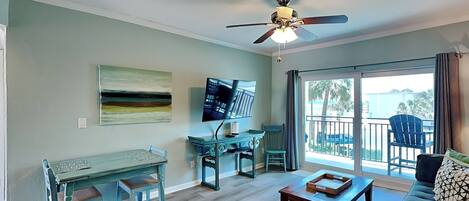 A living room with a sofa, coffee table, dining table, chairs, TV, ceiling fan, and large windows with a view.