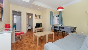 A living room with a sofa, a dining table with chairs, a TV, and a ceiling light.