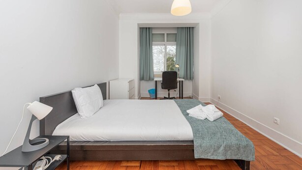 A modern bedroom with a bed, bedside table, lamp, and a desk with a chair.