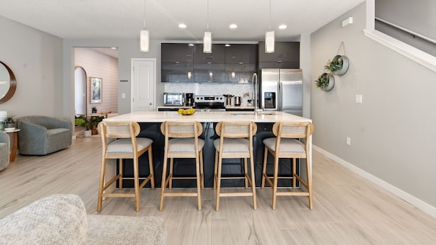 Una cocina moderna con una isla central, taburetes de bar, iluminación colgante y una zona de comedor con sofá.