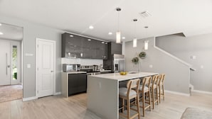 Una cocina moderna con armarios oscuros, una isla central con taburetes y una escalera que sube a otro nivel.