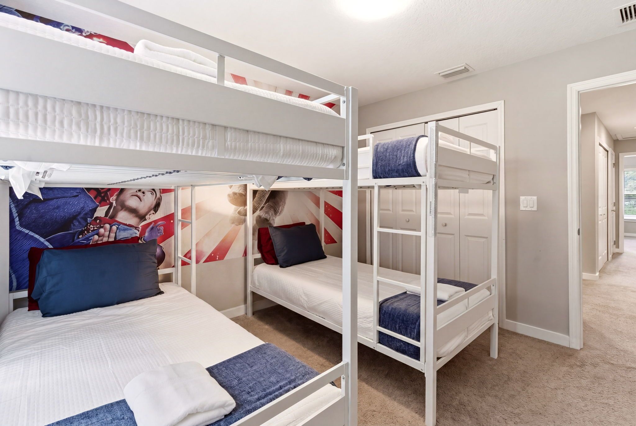 Une chambre avec un lit superposé, une affiche, un ours en peluche et une porte donnant sur une autre pièce.