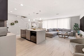 Eine moderne Küche mit integrierter Kochinsel, ein graues Sofa und ein Couchtisch in einem Wohnbereich.