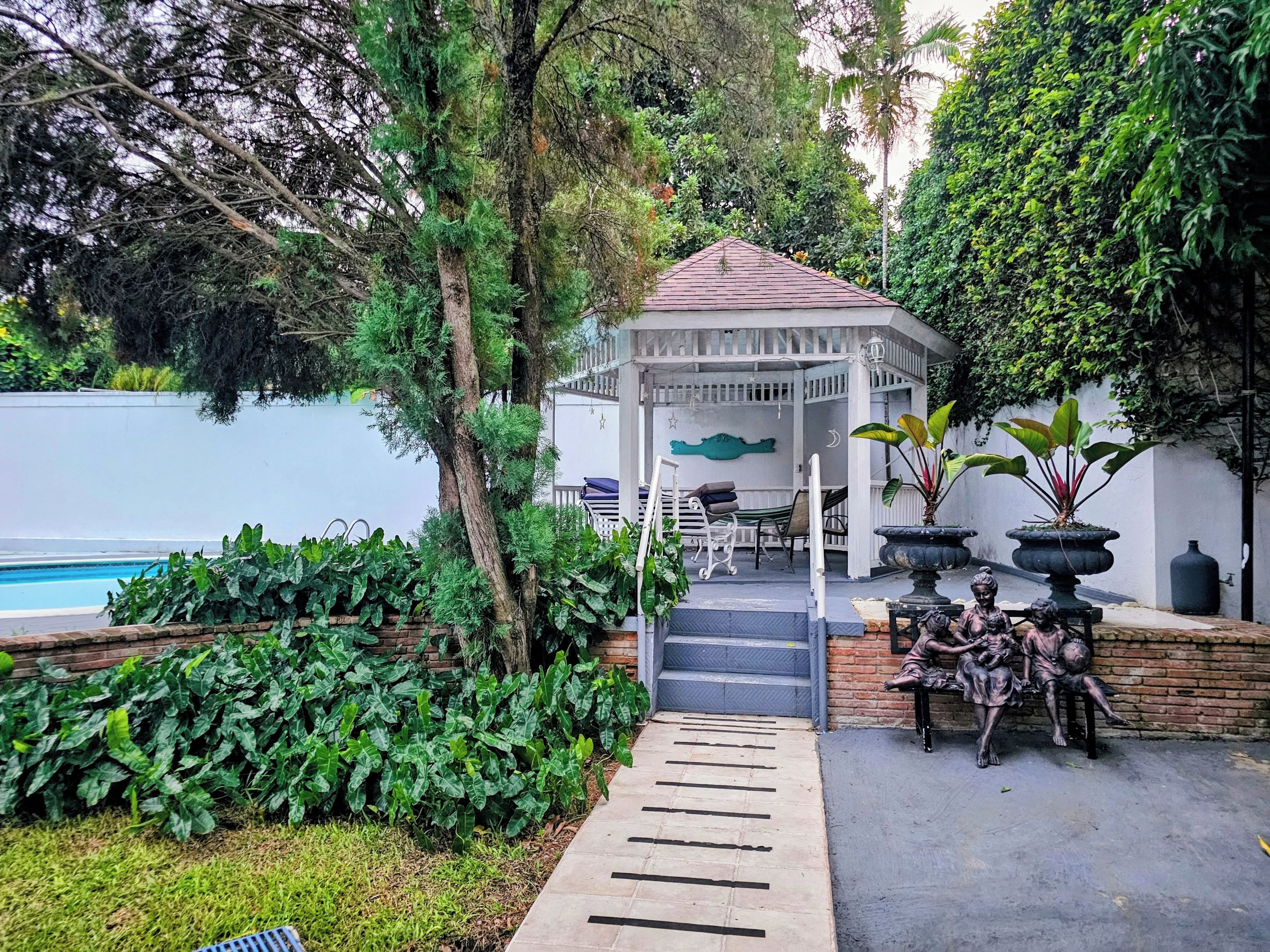 A gazebo with a tiled roof, surrounded by lush greenery and a swimming pool.