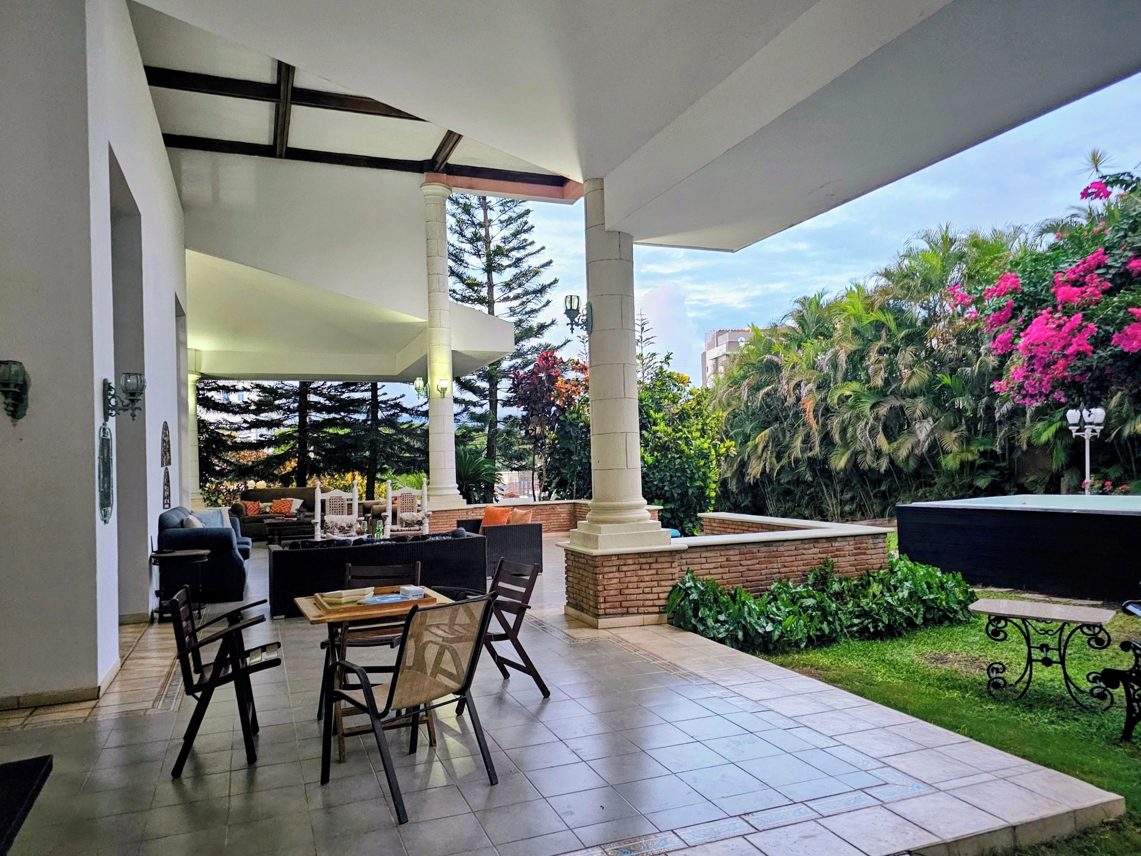 Une terrasse extérieure avec une table et des chaises, entourée de verdure et agrémentée d’une fontaine.