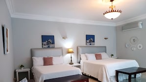 Ein Hotelzimmer mit zwei Betten, einem Schreibtisch, einer Bank, einer Lampe und Wandbildern.