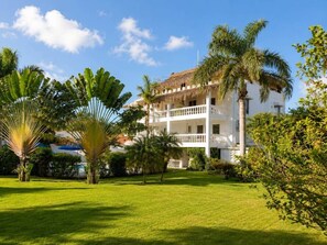 A white building with a balcony, surrounded by a well-maintained lawn and palm trees. - Modern Studio on Pedro Clisante with Pool (Sosúa)