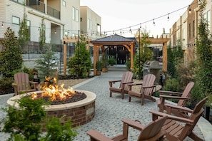 Ein Innenhof mit Feuerstelle, Gartenmöbeln, einer Pergola und einem Grill.