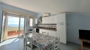 A compact kitchen with white cabinets, a dining table with a patterned tablecloth, and a television on a stand. - Scala dei Turchi Apartments Villa Saporito (Lido Rossello)