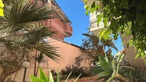 A paved pathway, green plants, and a building with a pink facade. - Scala dei Turchi Apartments Villa Saporito (Lido Rossello)