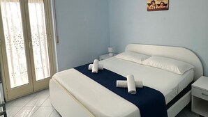 A bedroom with a bed, a nightstand, a window with curtains, and a painting on the wall. - Scala dei Turchi Apartments Villa Saporito (Lido Rossello)