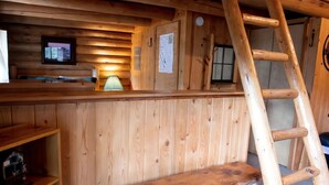 A wooden cabin interior with a wooden bench, a ladder, a desk with a lamp, and a framed picture on the wall. - Cowboy Log Cabin, Mountain views and Firepit (Bigfork)