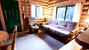 A log cabin interior with a sofa, armchair, and a green door. - Cowboy Log Cabin, Mountain views and Firepit (Bigfork)