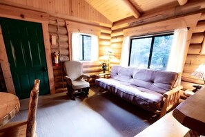 Ein Holzblockhaus-Innenraum mit einer Couch, einem Sessel und einer grünen Tür.