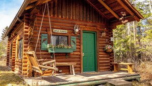 A log cabin with a swing chair, a green door, and a sign that reads 'Wild Flower.' - Experience Montana Cabins - 9 homes on 15 acres (Bigfork)
