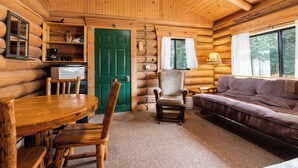 A log cabin interior with a dining table, chairs, a sofa, a lamp, and a green door. - Experience Montana Cabins - 9 homes on 15 acres (Bigfork)