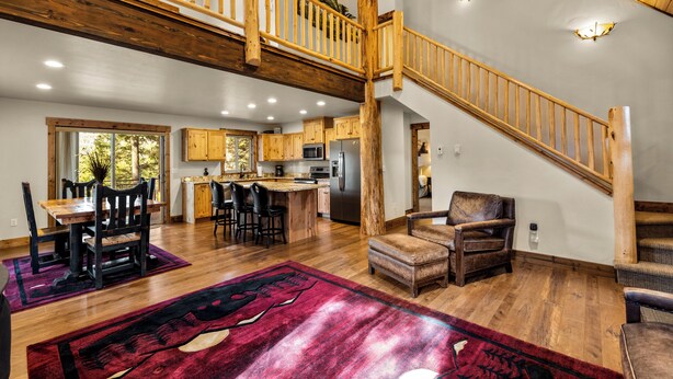 A spacious kitchen with wooden flooring, a dining area with a red rug, and a staircase with wooden railings. - Experience Montana Cabins - 9 homes on 15 acres (Bigfork)