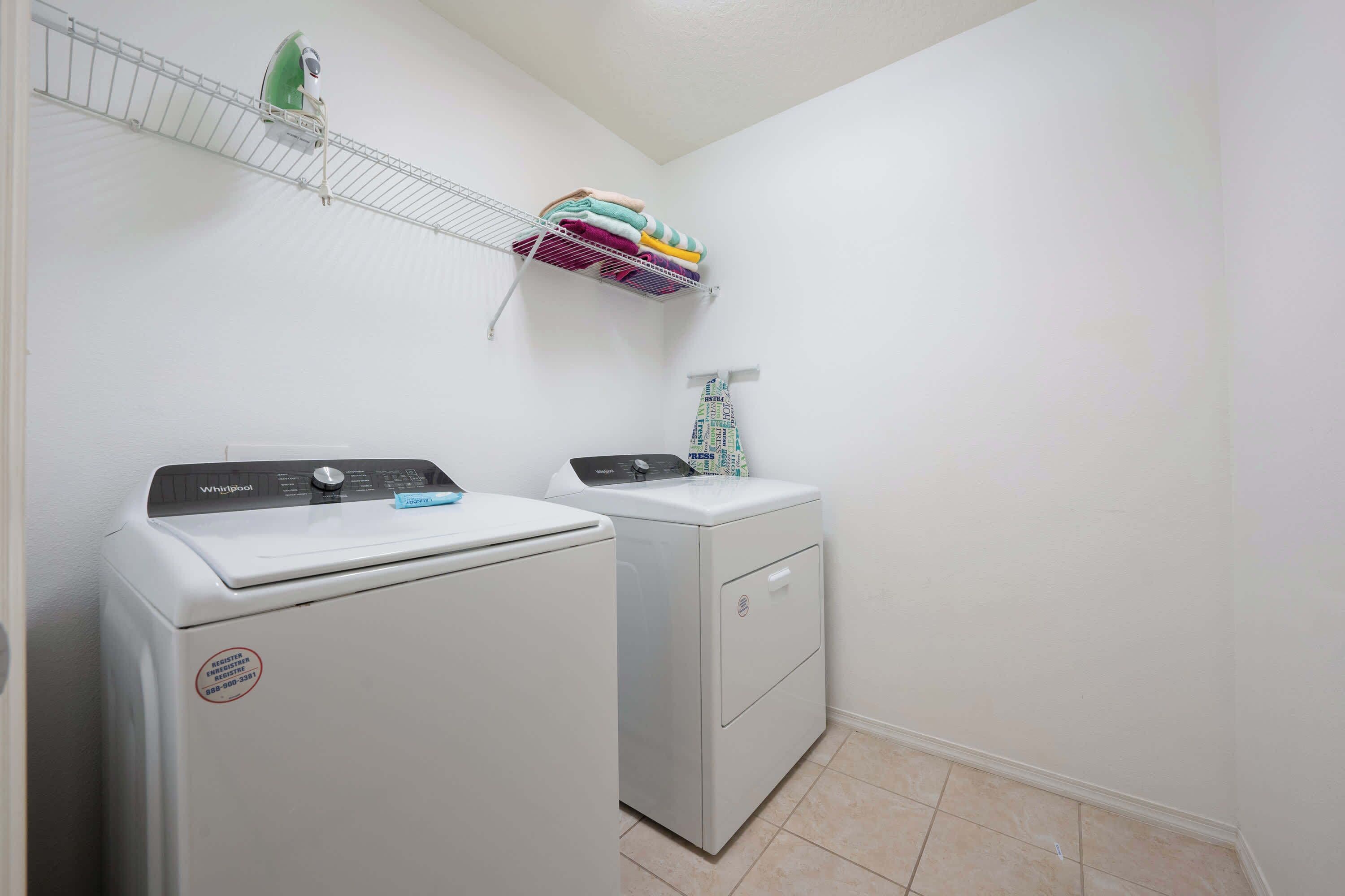 Une buanderie avec deux lave-linge et deux sèche-linge blancs, une étagère en métal où sont pliées des serviettes, et une serviette à motifs suspendue à un porte-serviettes.