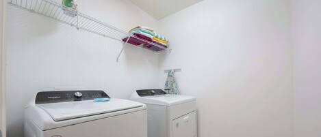 Une buanderie avec deux lave-linge et deux sèche-linge blancs, une étagère en métal où sont pliées des serviettes, et une serviette à motifs suspendue à un porte-serviettes.