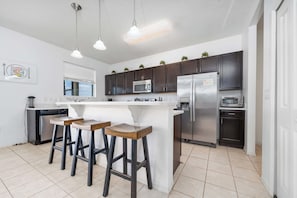 A modern kitchen with a central island, bar stools, stainless steel appliances, and pendant lighting.