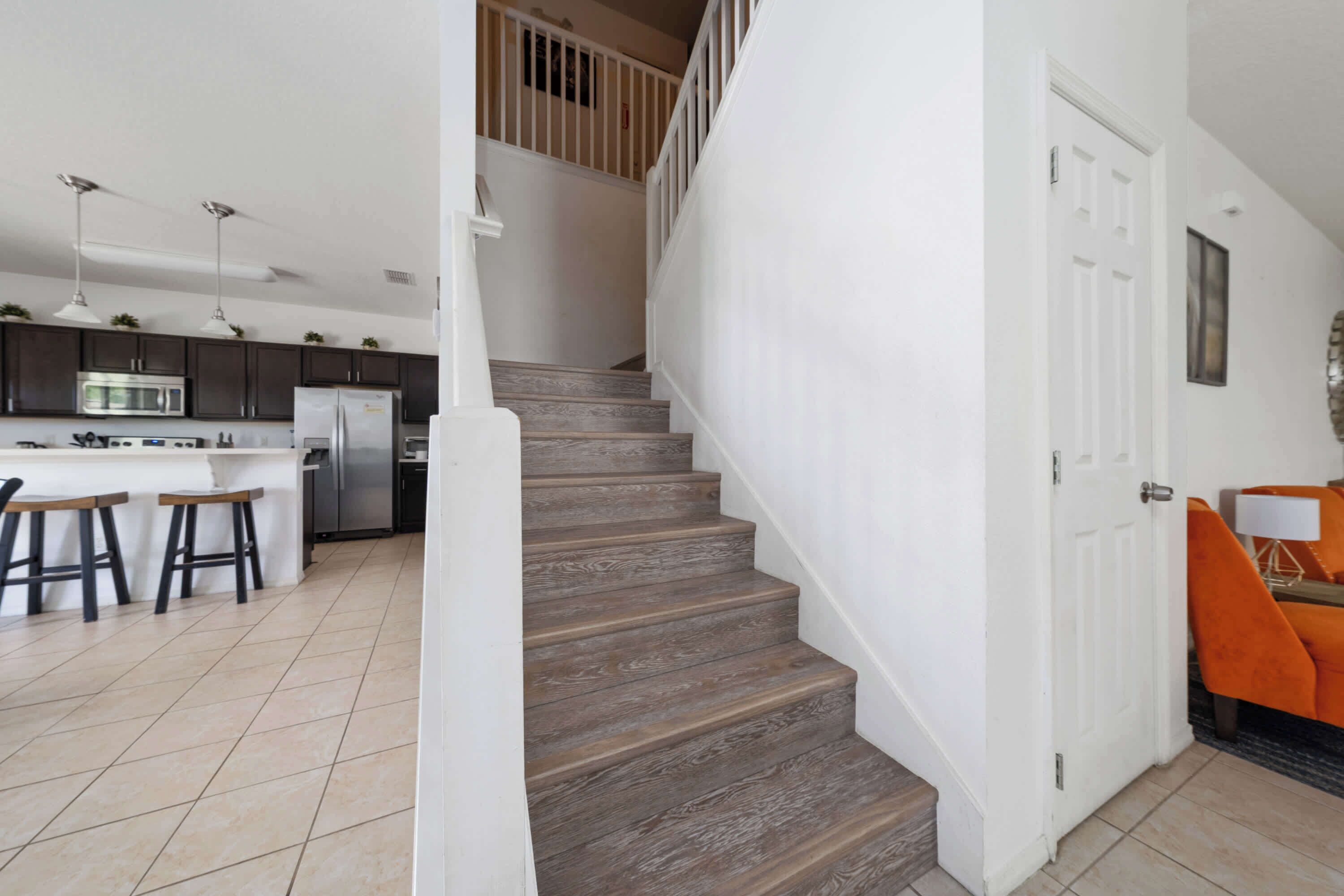A kitchen with dark cabinets, a white island with stools, and a staircase leading to a second floor.