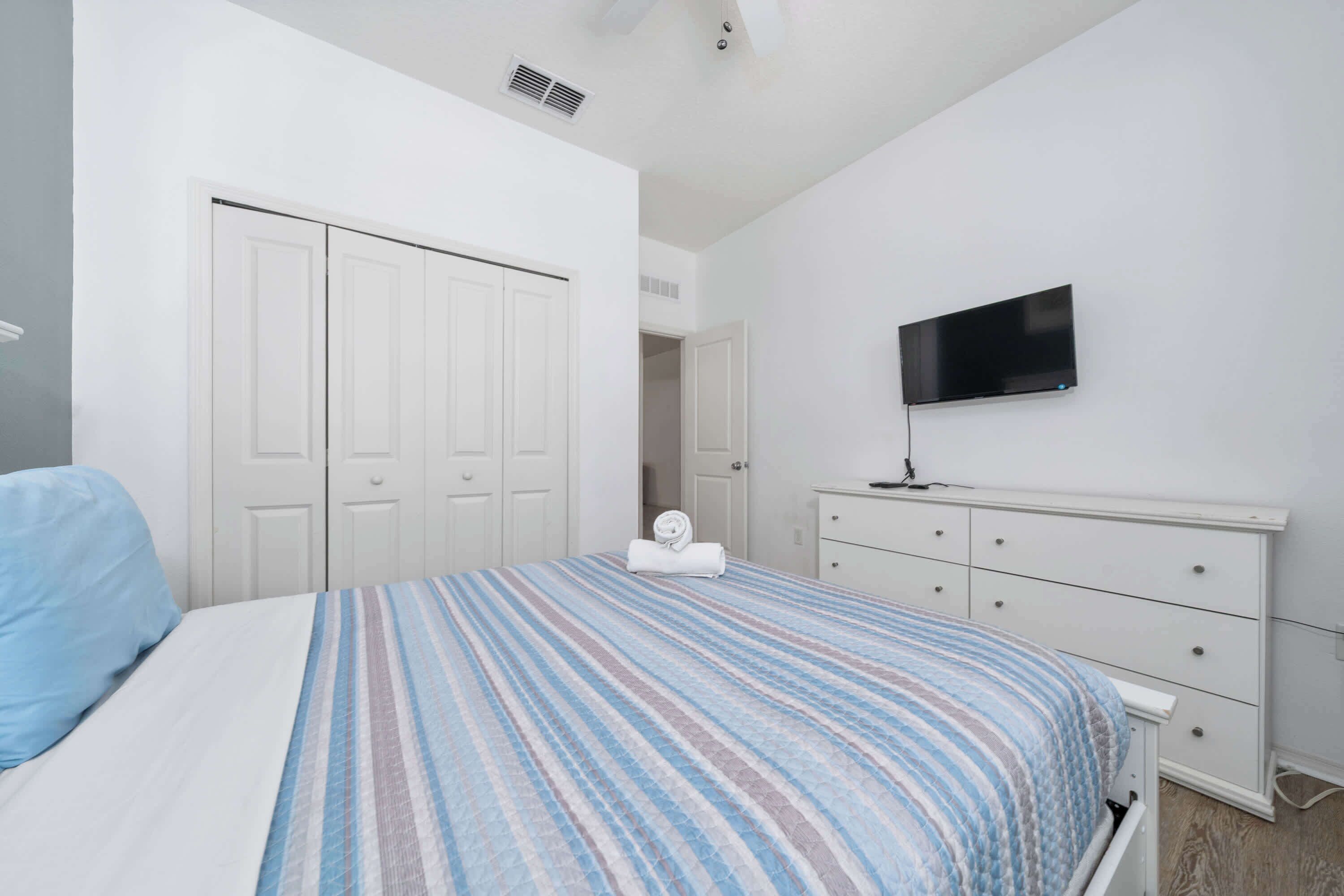 Un dormitorio con cama, televisor, cómoda y armario.