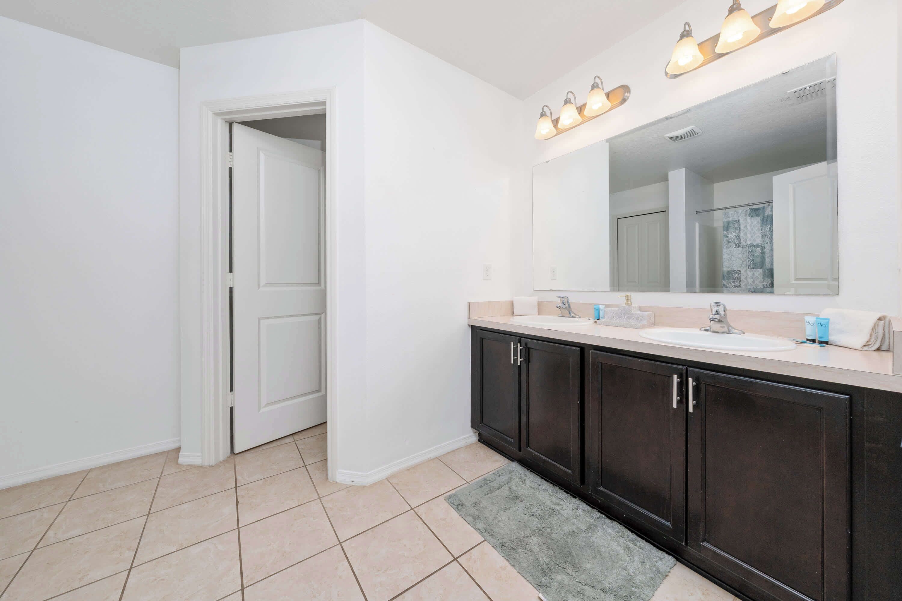 A bathroom with a white sink, dark cabinets, a large mirror, and a light fixture above the mirror.