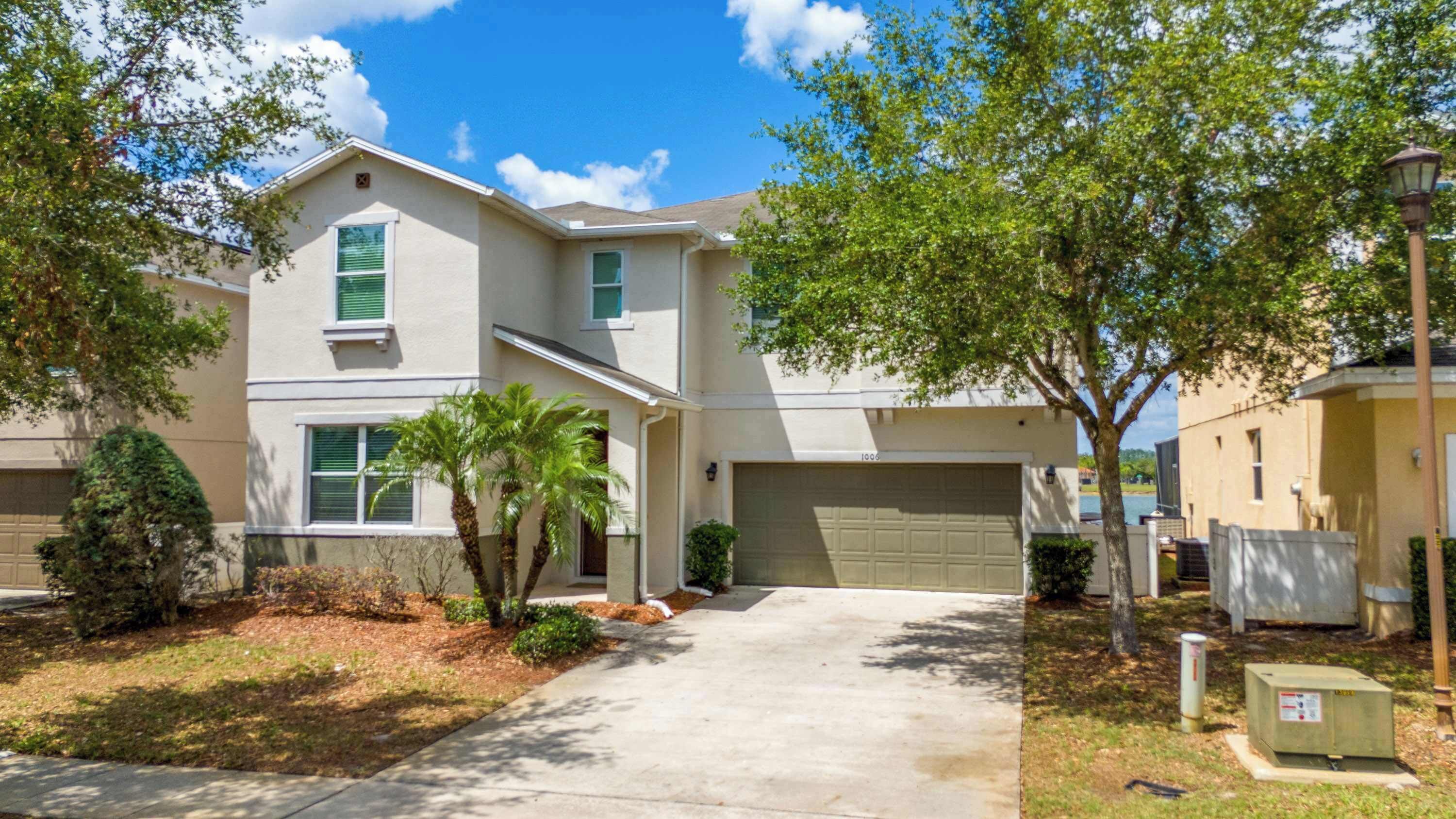 A two-story residential building with a garage, a driveway, and a well-maintained lawn with trees and shrubs.