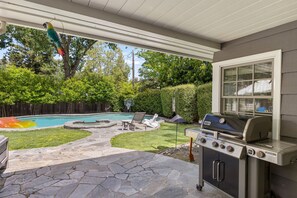 A backyard with a swimming pool, a barbecue grill, and a patio area with stone flooring.