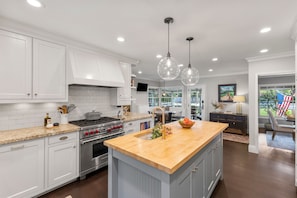 A kitchen with white cabinets, a large island, stainless steel appliances, and pendant lighting.