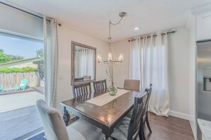 Un coin repas avec une table en bois, des chaises, un lustre et un grand miroir.