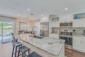 A modern kitchen with a marble countertop, stainless steel appliances, and a large island with bar stools. - Gathering Place Pool home Tampa/USF Bush Garden, Adventure Island and Moffit (Tampa)