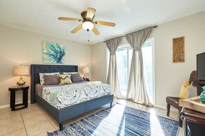 Ein Schlafzimmer mit einem Bett, zwei Nachttischen, einem Deckenventilator, einem Fenster mit Vorhängen und einem am Wand montierten Fernseher.