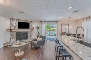 Ein geräumiges Wohnzimmer mit Kamin, einem darüber befestigten Fernseher und einer Essecke mit Bar.