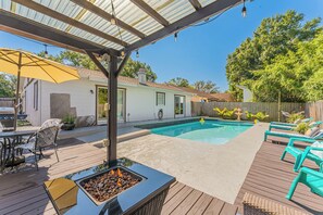Un jardin avec une piscine, un foyer extérieur, du mobilier de jardin et une terrasse couverte.