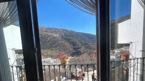 A balcony with potted plants, a clear view of a mountainous landscape, and a metal railing. - El Mirador Alto Apartment (Trevélez)