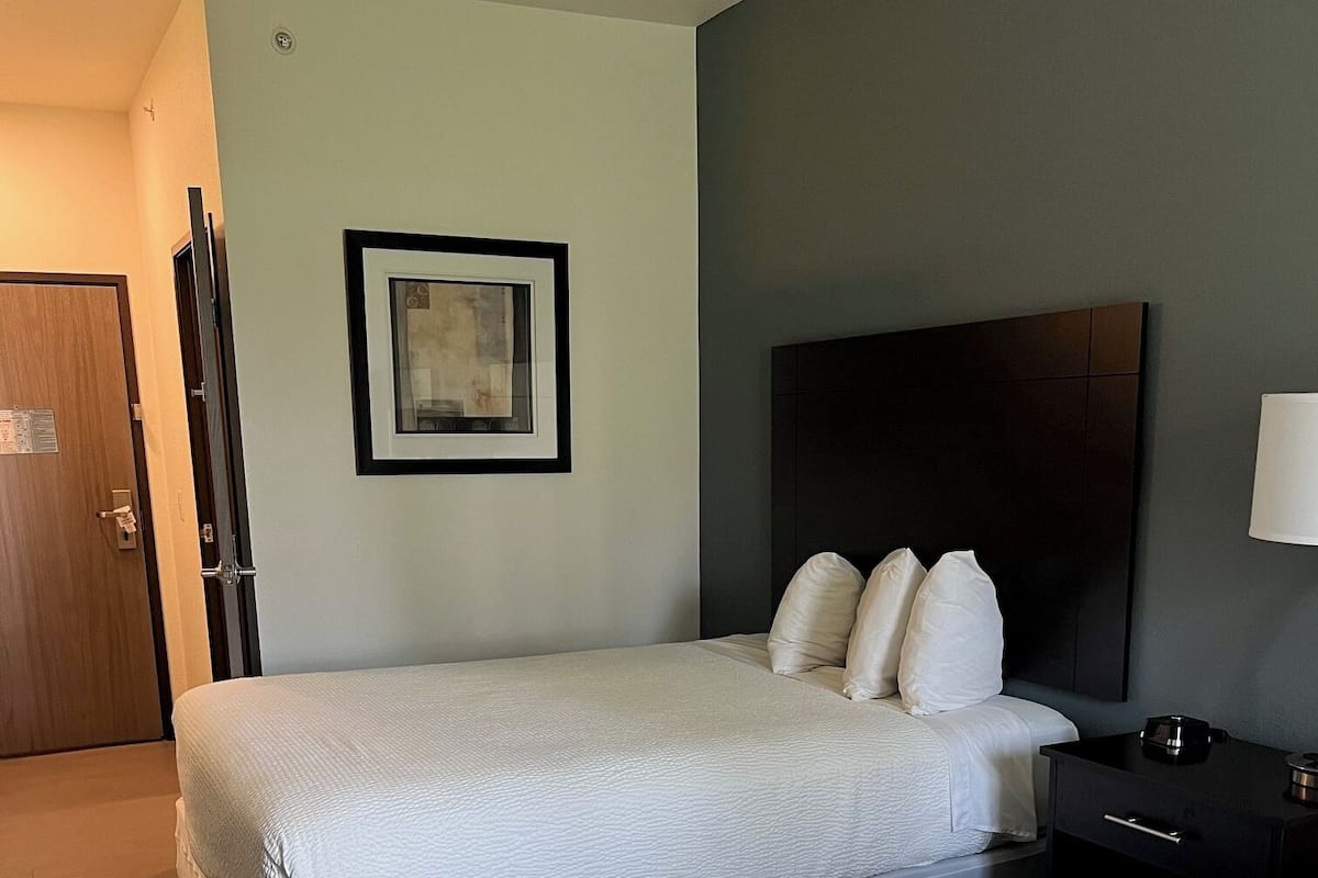 Una habitación de hotel con dos camas, un cuadro en la pared, una mesita de noche y una puerta.
