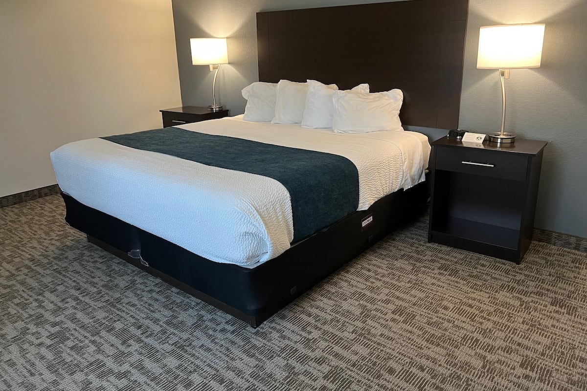 Habitación de hotel con una cama grande, dos mesitas de noche, un cabecero y dos lámparas fijadas a la pared.