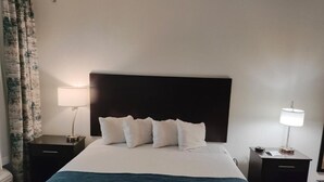 Une chambre d’hôtel avec un grand lit, deux tables de chevet, une tête de lit et une fenêtre avec des rideaux.