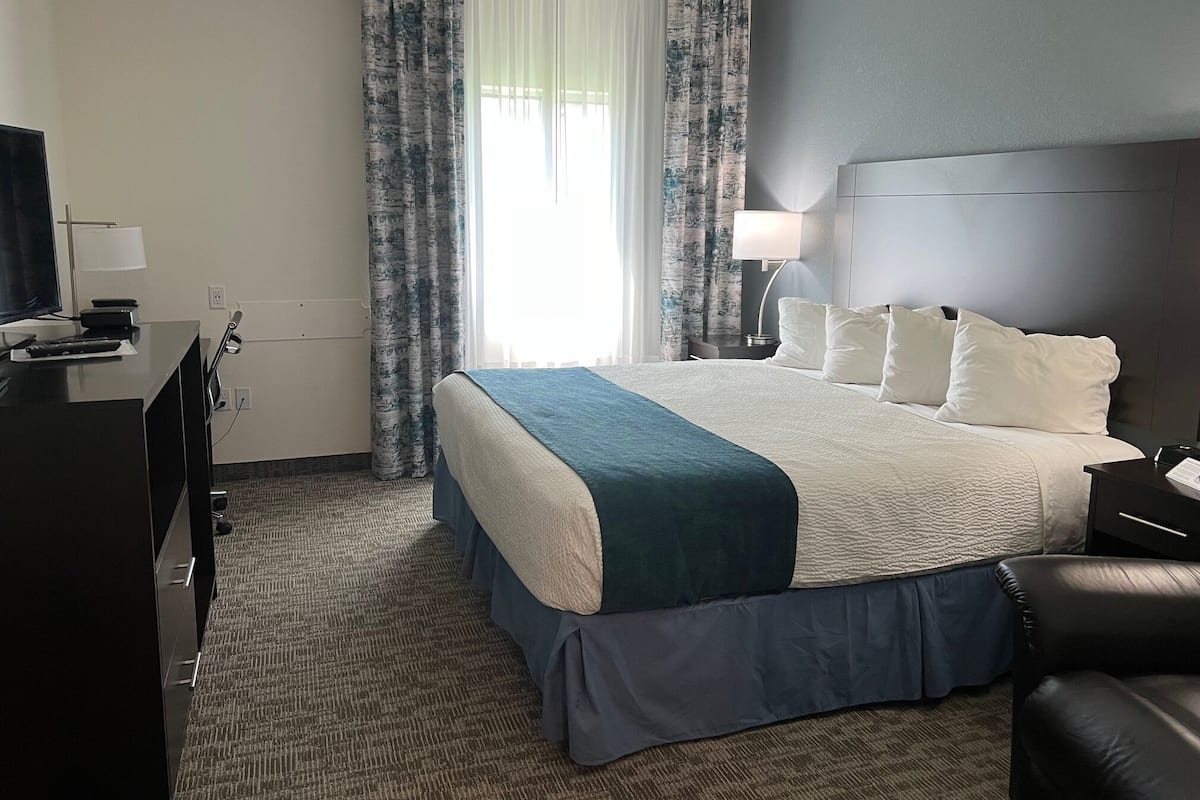 Una habitación de hotel con una cama, un escritorio con televisor, una lámpara y cortinas.