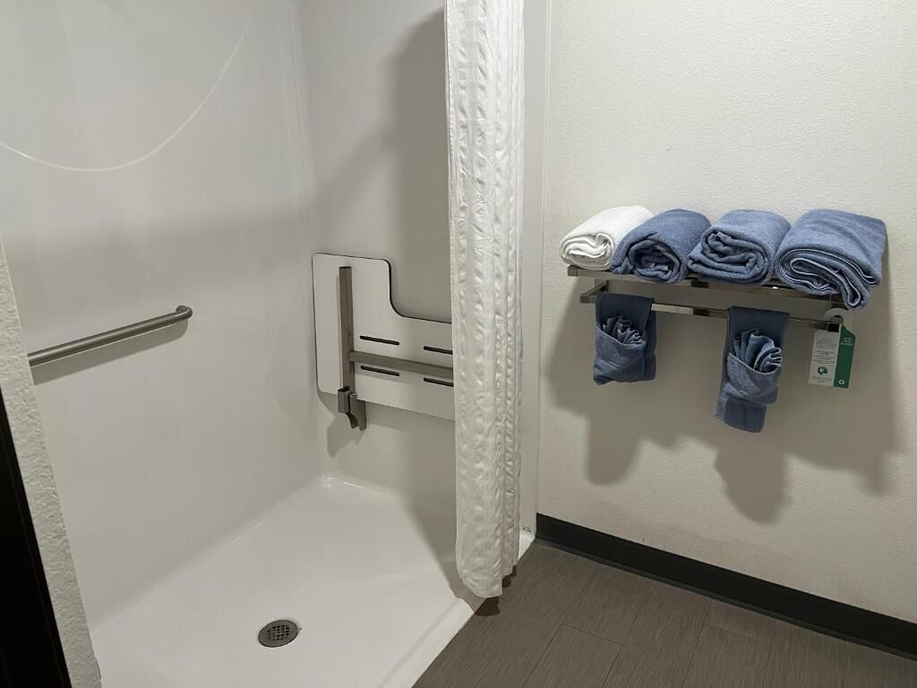 A bathroom with a shower, a towel rack with folded towels, and a handrail.