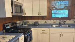 A kitchen with white cabinets, a microwave, a stove, a sink, and a window with a Red Rooster sign.