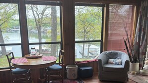 A room with a wooden table, chairs, a sofa, a rug, and large windows overlooking a body of water.