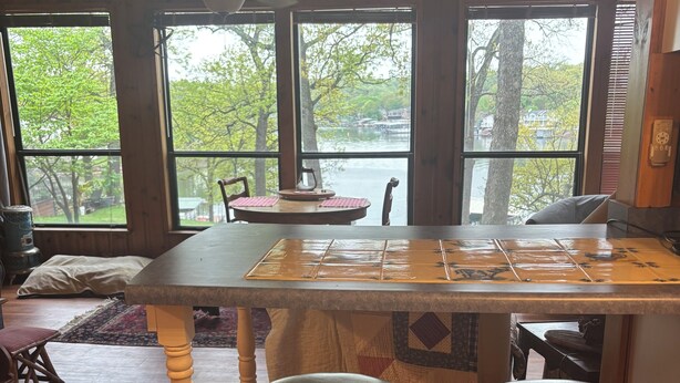 A kitchen with a wooden bar stool, a table, and large windows overlooking a body of water.