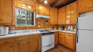 Una cocina con armarios de madera, estufa, refrigerador y ventana.